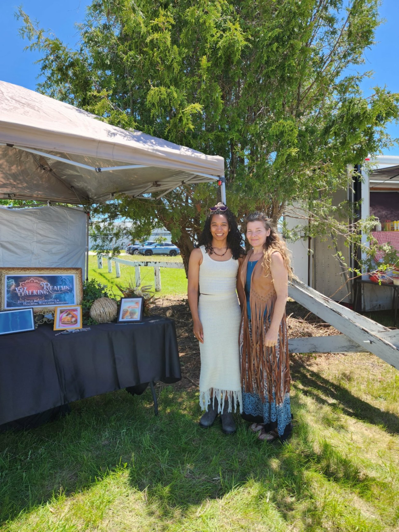 Natalie Daniel and Lisa Burwell standing together at the Walking Realms booth at Weco on a sunny day, with the Walking Realms sign displayed on the table beside them.