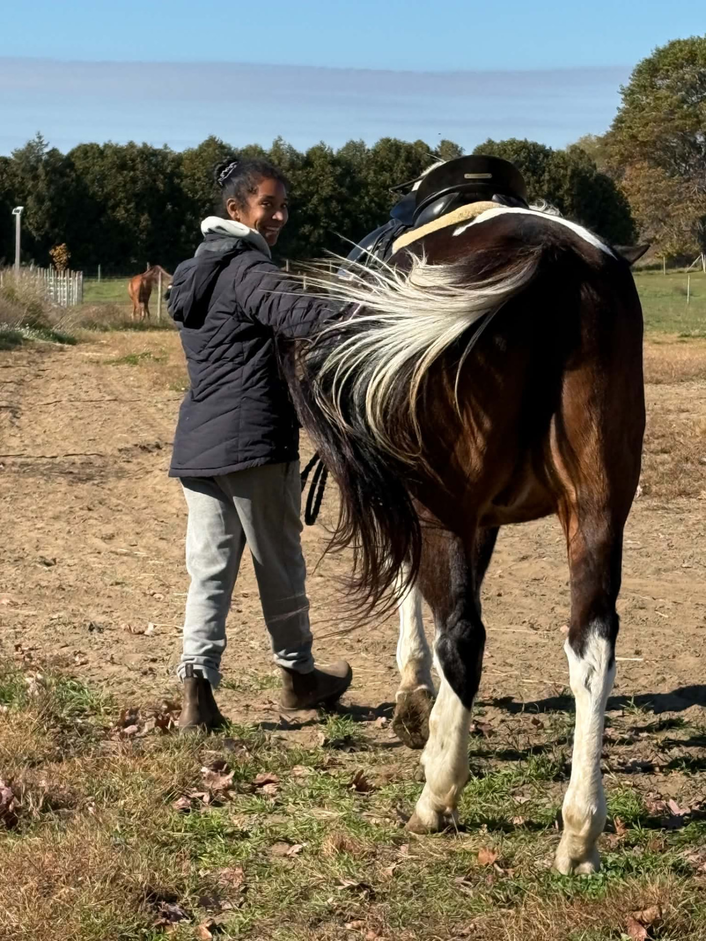 Natalie smiling over her shoulder as she walks with her saddled horse
