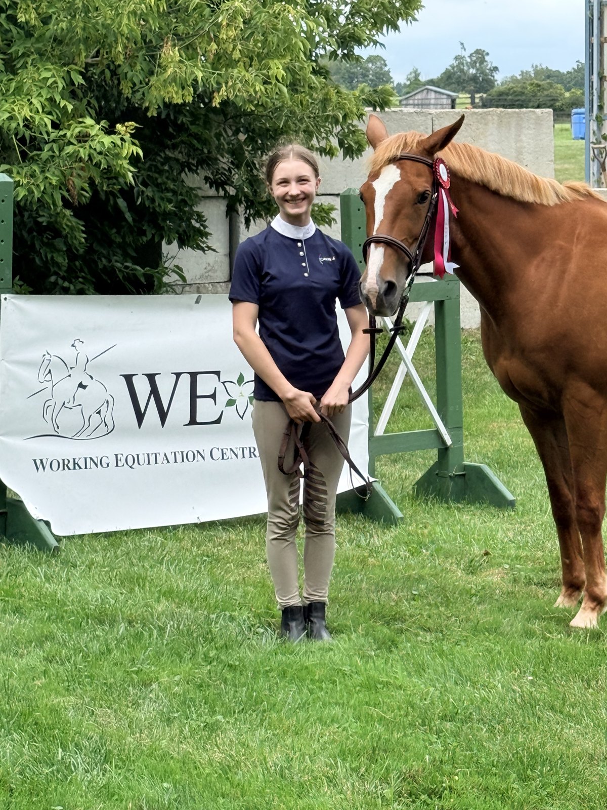 A young rider standing with her chestnut horse and a ribbon at the working equitation show at Sprucehaven Farm